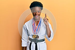 Young african american girl wearing karate kimono and black belt pointing finger up with successful idea