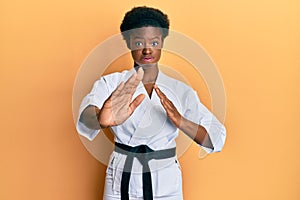 Young african american girl wearing karate kimono and black belt puffing cheeks with funny face