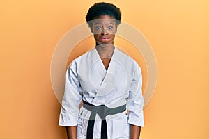 Young african american girl wearing karate kimono and black belt puffing cheeks with funny face
