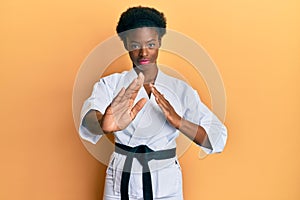 Young african american girl wearing karate kimono and black belt relaxed with serious expression on face