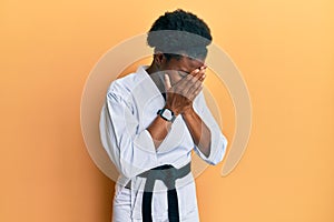 Young african american girl wearing karate kimono and black belt with sad expression covering face with hands while crying