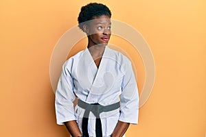 Young african american girl wearing karate kimono and black belt smiling looking to the side and staring away thinking