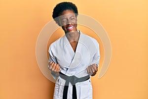 Young african american girl wearing karate kimono and black belt very happy and excited doing winner gesture with arms raised,