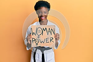 Young african american girl wearing karate kimono holding woman power banner looking positive and happy standing and smiling with