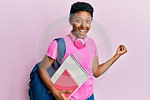 Young african american girl wearing school bag and holding books screaming proud, celebrating victory and success very excited