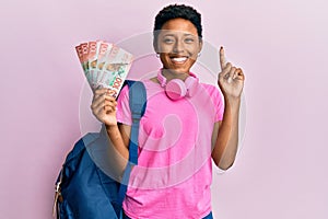 Young african american girl wearing student backpack and holding new zealand dollars smiling with an idea or question pointing