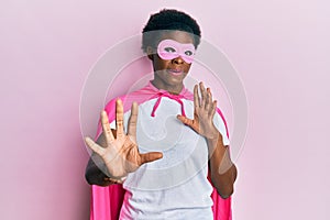Young african american girl wearing superhero mask and cape costume afraid and terrified with fear expression stop gesture with