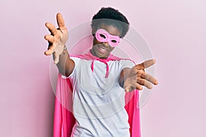 Young african american girl wearing superhero mask and cape costume looking at the camera smiling with open arms for hug