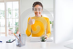 Young african american girl working using computer happy with big smile doing ok sign, thumb up with fingers, excellent sign