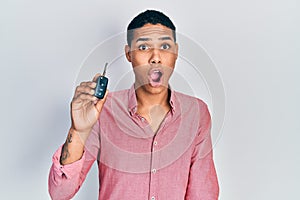 Young african american guy holding key of new car scared and amazed with open mouth for surprise, disbelief face