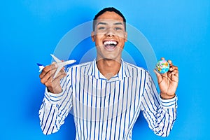 Young african american guy holding paper plane and world ball smiling and laughing hard out loud because funny crazy joke