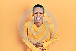 Young african american guy listening to music using headphones smiling and laughing hard out loud because funny crazy joke with