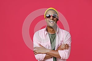 Young African-American guy, man in UK, Great Britain flag sunglasses, standing with arms folded wearing pink shirt and