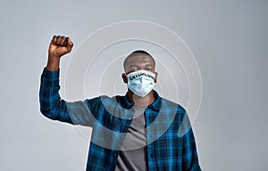 Young african american guy wearing protective mask with inscription BLM looking at camera, while posing with raised fist