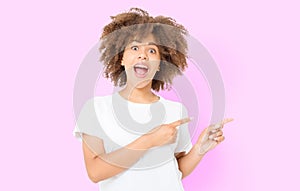 Young african american happy woman showing copyspace pointing on isolated pink background. Summer fun. Template, blank shirt. Afro