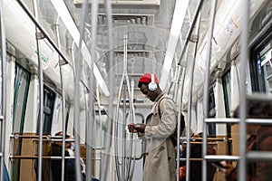 Black hipster man wear wireless headphones, listening to the music, using smartphone in subway train