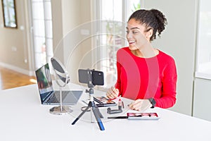 Young african american influencer woman recording make up tutorial looking away to side with smile on face, natural expression