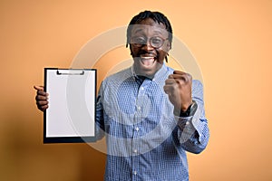 Young african american inspector man wearing glasses holding clipboard checklist screaming proud and celebrating victory and