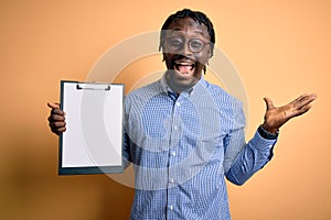 Young african american inspector man wearing glasses holding clipboard checklist very happy and excited, winner expression
