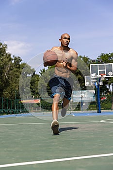 Young african-american male basketball player training at street public stadium, sport court or palyground outdoors