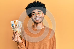 Young african american man with afro hair holding 500 philippine peso banknotes looking positive and happy standing and smiling