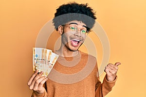 Young african american man with afro hair holding 500 philippine peso banknotes pointing thumb up to the side smiling happy with