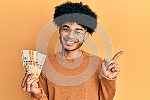 Young african american man with afro hair holding 500 philippine peso banknotes smiling happy pointing with hand and finger to the