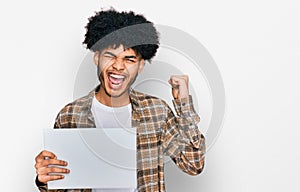 Young african american man with afro hair holding blank empty banner screaming proud, celebrating victory and success very excited