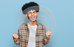 Young african american man with afro hair wearing casual clothes excited for success with arms raised and eyes closed celebrating