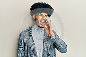 Young african american man with afro hair wearing casual clothes  glasses shouting and screaming loud to side with hand on mouth