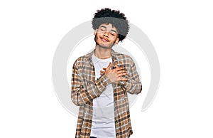 Young african american man with afro hair wearing casual clothes smiling with hands on chest with closed eyes and grateful gesture