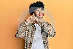 Young african american man with afro hair wearing casual clothes smiling in love doing heart symbol shape with hands