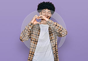 Young african american man with afro hair wearing casual clothes smiling in love doing heart symbol shape with hands