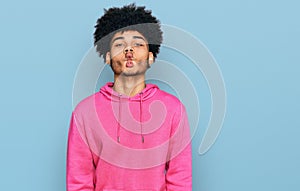 Young african american man with afro hair wearing casual pink sweatshirt making fish face with lips, crazy and comical gesture