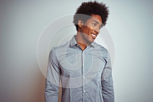 Young african american man with afro hair wearing grey shirt over isolated white background looking away to side with smile on