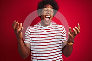 Young african american man with afro hair wearing striped t-shirt over isolated red background celebrating mad and crazy for