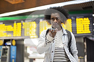 Young African American man with afro hairstyle talking on the phone. He is in an airport terminal