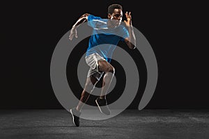 Young African-American man, athlete training isolated over black background.