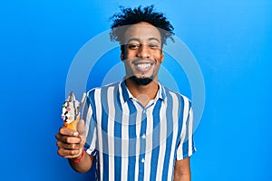 Young african american man with beard eating ice cream looking positive and happy standing and smiling with a confident smile