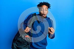 Young african american man with beard holding gym bag scared and amazed with open mouth for surprise, disbelief face