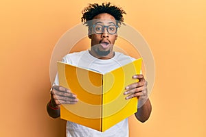Young african american man with beard reading a book wearing glasses afraid and shocked with surprise and amazed expression, fear