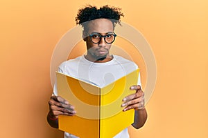 Young african american man with beard reading a book wearing glasses depressed and worry for distress, crying angry and afraid