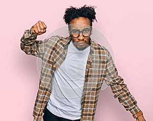 Young african american man with beard wearing casual clothes and glasses angry and mad raising fist frustrated and furious while