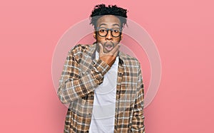 Young african american man with beard wearing casual clothes and glasses looking fascinated with disbelief, surprise and amazed