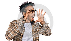 Young african american man with beard wearing casual clothes and glasses shouting angry out loud with hands over mouth