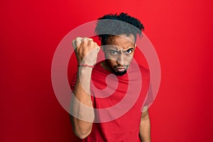 Young african american man with beard wearing casual red t shirt angry and mad raising fist frustrated and furious while shouting