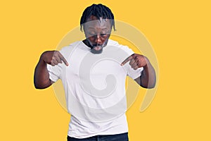 Young african american man with braids wearing casual white tshirt pointing down with fingers showing advertisement, surprised