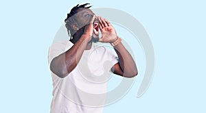 Young african american man with braids wearing casual white tshirt shouting angry out loud with hands over mouth