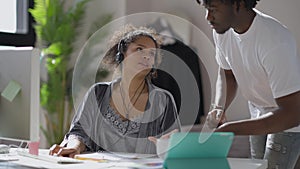 Young African American man bringing coffee cup for tired overworking woman messaging online from home office. Exhausted