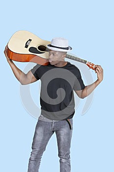 Young African American man carrying guitar over light blue background